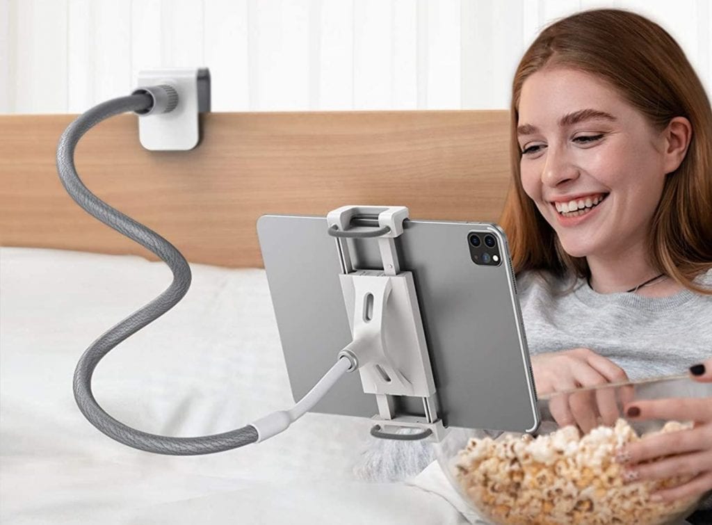 mujer en su cama mientras ve una película en su tablet sostenida por un soporte de brazo